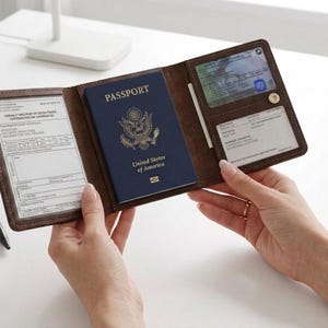 May include: A dark brown leather passport holder featuring a central slot for a United States passport, a clear plastic window for an identification card, and additional transparent sleeves for travel documents and vaccination records.