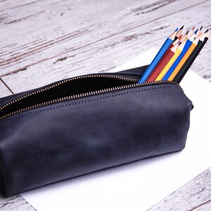 Peut inclure: Une trousse &agrave; crayons en cuir bleu fonc&eacute; avec une fermeture &agrave; glissi&egrave;re. La trousse est remplie de crayons de couleur.