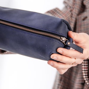Peut inclure: Une pochette zipp&eacute;e en cuir bleu fonc&eacute; avec un tirette de fermeture &eacute;clair dor&eacute;e et une petite sangle en cuir.