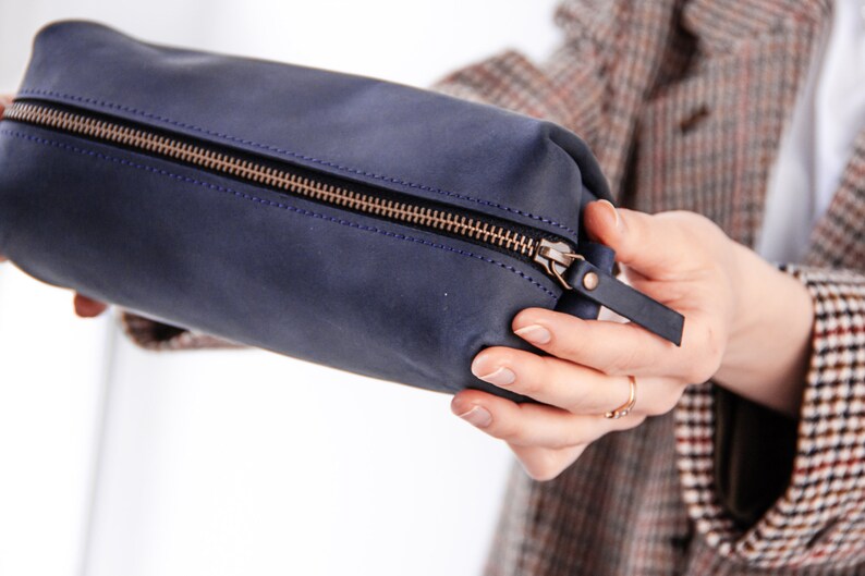 Peut inclure: Une pochette zipp&eacute;e en cuir bleu fonc&eacute; avec un tirette de fermeture &eacute;clair dor&eacute;e et une petite sangle en cuir.