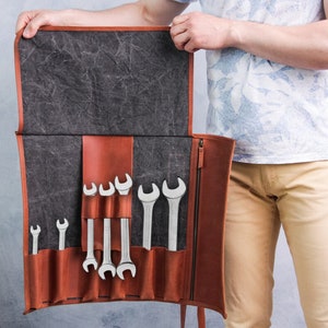 May include: A brown leather tool roll with a gray canvas flap, open to reveal a set of wrenches in various sizes.