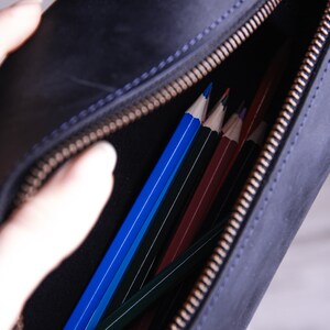 Peut inclure: Une trousse &agrave; crayons en cuir noir avec une fermeture &agrave; glissi&egrave;re. La trousse est ouverte et remplie de crayons de couleur.