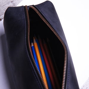 Peut inclure: Une trousse &agrave; crayons en cuir noir avec une ouverture &agrave; glissi&egrave;re, r&eacute;v&eacute;lant une vari&eacute;t&eacute; de crayons de couleur &agrave; l'int&eacute;rieur.