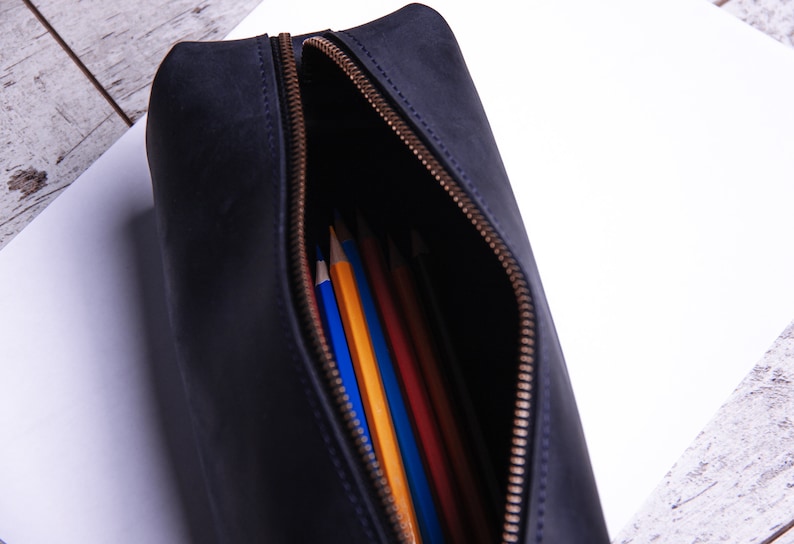 Peut inclure: Une trousse &agrave; crayons en cuir noir avec une ouverture &agrave; glissi&egrave;re, r&eacute;v&eacute;lant une vari&eacute;t&eacute; de crayons de couleur &agrave; l'int&eacute;rieur.
