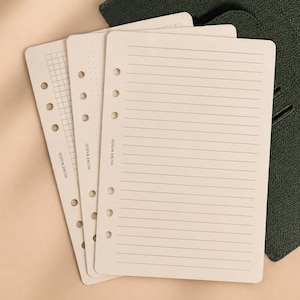 May include: Three off-white planner refill pages with six punched holes along the left side. The pages feature different layouts: one with horizontal lines, one with a dot grid, and one with a square grid. Each page is printed with the text HUMEWOOD.