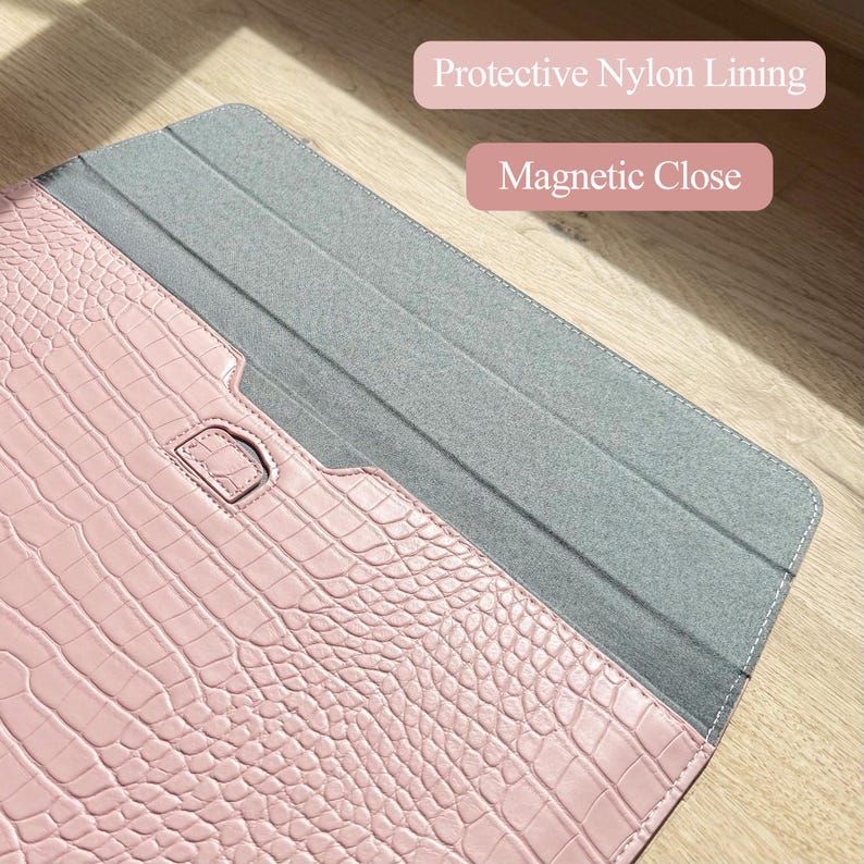 Op de afbeelding: Een roze laptophoes van imitatiekrokodillenleer met een grijze nylon voering en magnetische sluiting. De hoes is open en onthult de binnenvoering. Tekst op de afbeelding luidt "Protective Nylon Lining" en "Magnetic Close."