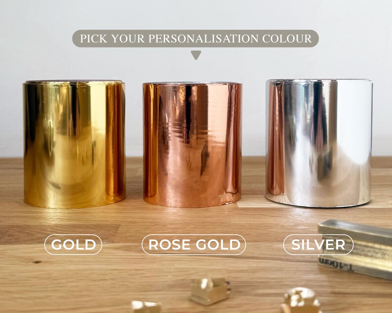 K&ouml;nnte beinhalten: Drei zylindrische Metallbeh&auml;lter in Gold, Ros&eacute;gold und Silber. &Uuml;ber den Beh&auml;ltern steht der Text "PICK YOUR PERSONALISATION COLOUR". Darunter stehen die W&ouml;rter "GOLD", "ROSE GOLD" und "SILVER".