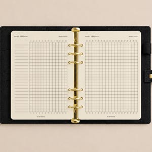 Può includere: Un raccoglitore nero con texture in pelle e un meccanismo a sei anelli dorati contenente pagine color crema per il monitoraggio delle abitudini. Le pagine presentano una griglia per gennaio 2026, numerata da 1 a 31, con il testo HABIT TRACKER e ELMEWOOD.