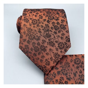 May include: A brown silk tie with a black floral pattern. The tie comes with a matching pocket square.