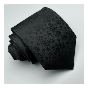 May include: A black silk tie with a subtle floral pattern. The tie is rolled up and ready to be worn.