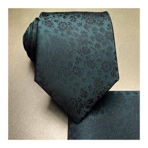 May include: A dark green patterned silk tie with a matching pocket square. The tie has a floral pattern in a darker shade of green.