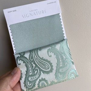 May include: A fabric swatch card with the text "Galina Signature" and the fabric names "Dusty Sage" and "Charmeuse". The card shows two fabric swatches, one in a solid dusty sage green color and the other in a paisley pattern with a white background and green paisley designs.