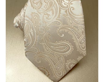 May include: A beige paisley patterned necktie. The tie features a repeating design of curved, teardrop-shaped motifs in a lighter shade of beige. The tie is knotted and displayed on a neutral background, showcasing its intricate pattern and color.
