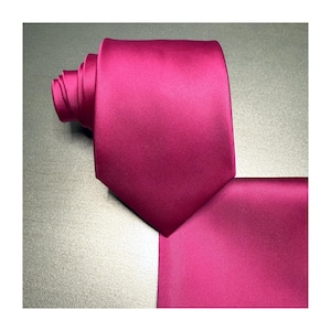 May include: A rolled-up magenta tie and matching pocket square. The tie is folded and has a pointed end. The pocket square is square and lies flat. Both items are made of a smooth, shiny fabric.