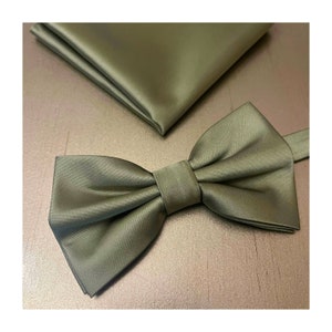 May include: A sage green bow tie made of satin fabric. The bow tie is tied and ready to wear.