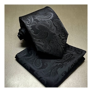 May include: A black paisley patterned tie and pocket square set. The tie and pocket square are made of a smooth, silky fabric.
