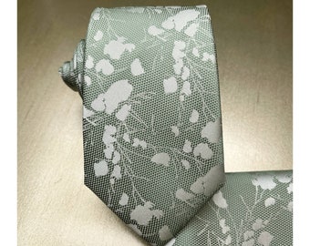 Könnte beinhalten: Eine grüne gemusterte Krawatte mit einem weißen Blumenmuster. Die Krawatte ist aus seidenartigem Material und hat einen dezenten Glanz.