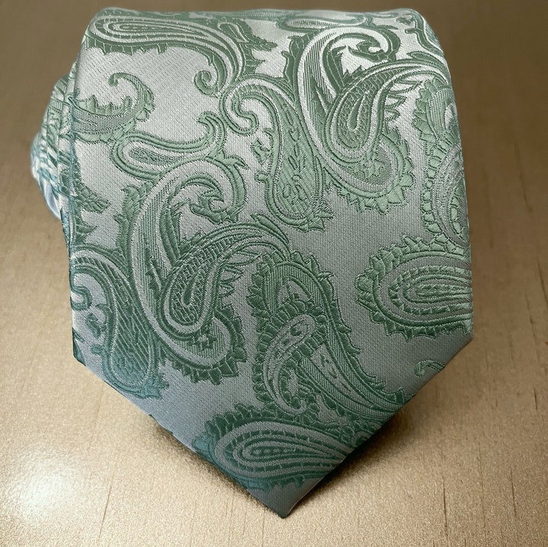 May include: A green and white paisley patterned tie. The tie has a light green background with a white paisley pattern.