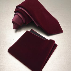 May include: A burgundy velvet pocket square and a burgundy velvet tie. The pocket square has a black border.
