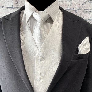 May include: A white paisley patterned waistcoat and matching bow tie and pocket square. The waistcoat has a button closure and the bow tie is tied.