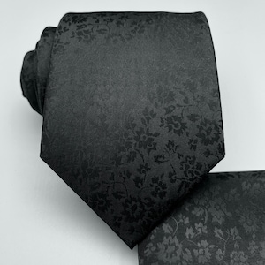 May include: A black silk tie with a subtle floral pattern. The pattern is a dark gray color and is evenly distributed throughout the tie.