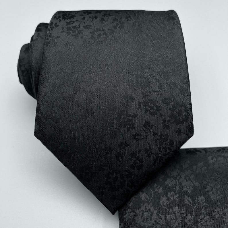 May include: A black silk tie with a subtle floral pattern. The pattern is a dark gray color and is evenly distributed throughout the tie.