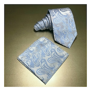 Peut inclure: Un ensemble de cravate et de mouchoir de poche à motif paisley bleu clair. La cravate est pliée et le mouchoir de poche est posé à plat.