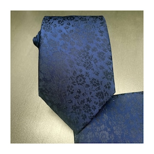 May include: A navy blue tie and pocket square set. The tie and pocket square feature a floral pattern in a darker shade of blue. The tie is knotted, and the pocket square is neatly folded.