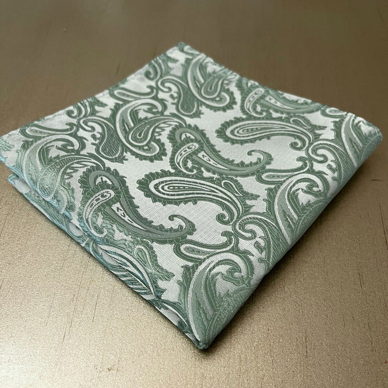 May include: A green paisley pocket square with a white background. The paisley pattern is intricate and detailed.