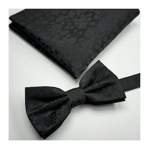 May include: A black bow tie with a floral pattern. The bow tie is made of a soft, textured fabric.