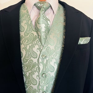 May include: A green paisley patterned vest with a white background. The vest is worn over a white dress shirt with a green paisley patterned tie.