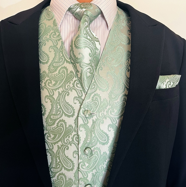 May include: A green paisley patterned vest with a white background. The vest is worn over a white dress shirt with a green paisley patterned tie.