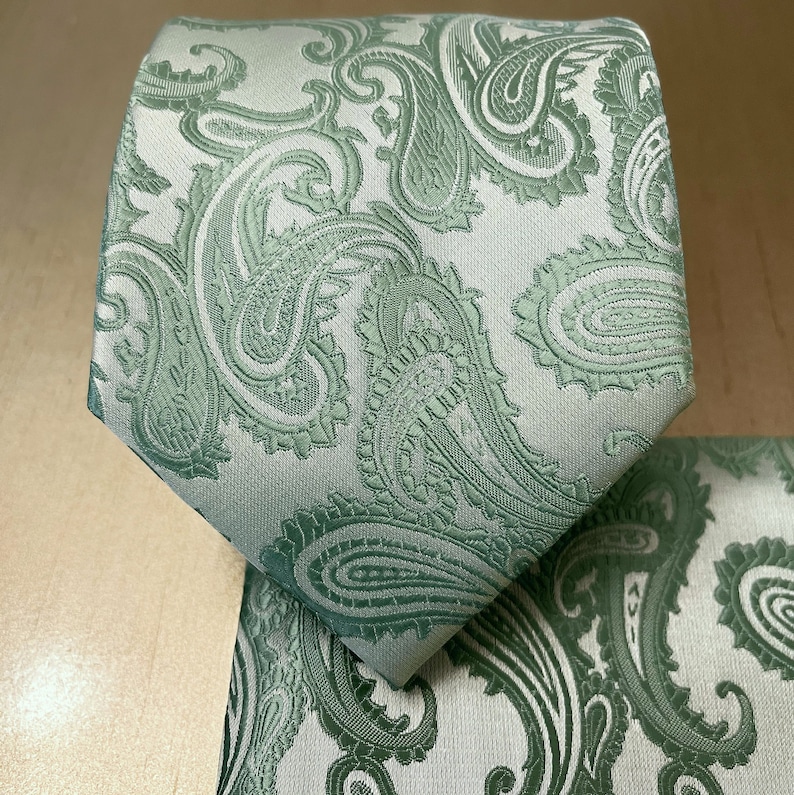 May include: A green paisley patterned tie with a white background. The tie is made of a silky material and has a classic design.