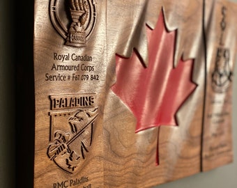 May include: A wooden plaque featuring a carved Canadian flag, the Royal Canadian Armoured Corps crest, and the text "Royal Canadian Armoured Corps, Service # F67 079 842, Paladins, RMC Paladins Mens Volleyball Team Captain 2021/22".
