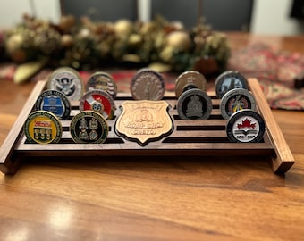 Op de afbeelding: Een houten display met sleuven om challenge-munten te bewaren. De display heeft een houten schild met de tekst "RCMP GRC C870" in het midden. De display is gevuld met verschillende challenge-munten, waaronder een munt van het Canadian Police College met een esdoornblad en de tekst "CPC CCP 2022".