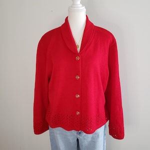 May include: A red cardigan with a shawl collar and gold buttons. The cardigan has a crocheted trim around the bottom and sleeves.