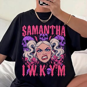 May include: A black t-shirt featuring a graphic print of a blonde character with pigtails, fangs, and an angry expression. The design includes the text SAMANTHA and I W K Y M, surrounded by purple and pink skulls and lightning bolt accents.