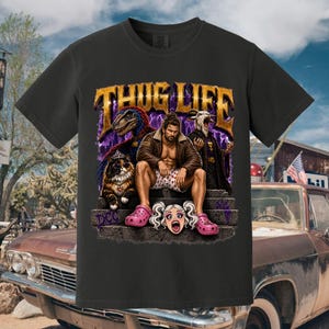 May include: A black t-shirt featuring a graphic print with the text THUG LIFE in gold letters. The design includes a central figure in a brown jacket and patterned shorts, a dinosaur, a cat with a crown, a goat, and a stylized face with pigtails.