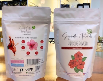 May include: Two white pouches of Sugandh Naturals Hibiscus Powder. One pouch displays the benefits of using hibiscus, with a pink hibiscus flower graphic. The other pouch features the text "Hibiscus Powder" and a floral illustration.