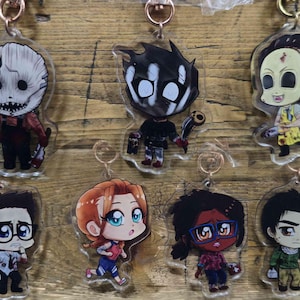 May include: A collection of acrylic keychains featuring cartoon characters with various designs. The keychains have a clear background and gold-colored metal rings. The characters are depicted in a chibi style, with exaggerated features and vibrant colors.