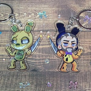 May include: Two acrylic keychains featuring cartoon characters, each holding a knife. One is a green rabbit with a sinister grin, the other a man with a beard and glasses. Both have silver key rings.