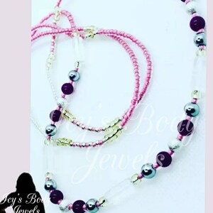 May include: A collection of beaded body jewelry in shades of pink, silver, and dark purple. The jewelry includes strands of small pink beads, larger silver beads, and dark purple beads. Some strands have clear, rectangular beads.