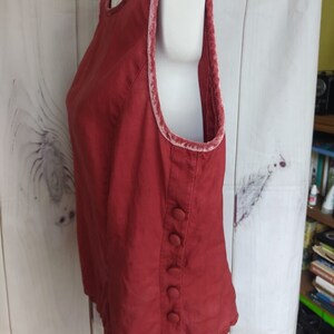 May include: A sleeveless, burgundy top with a velvet trim around the neckline and armholes. The top has a button closure on the side.