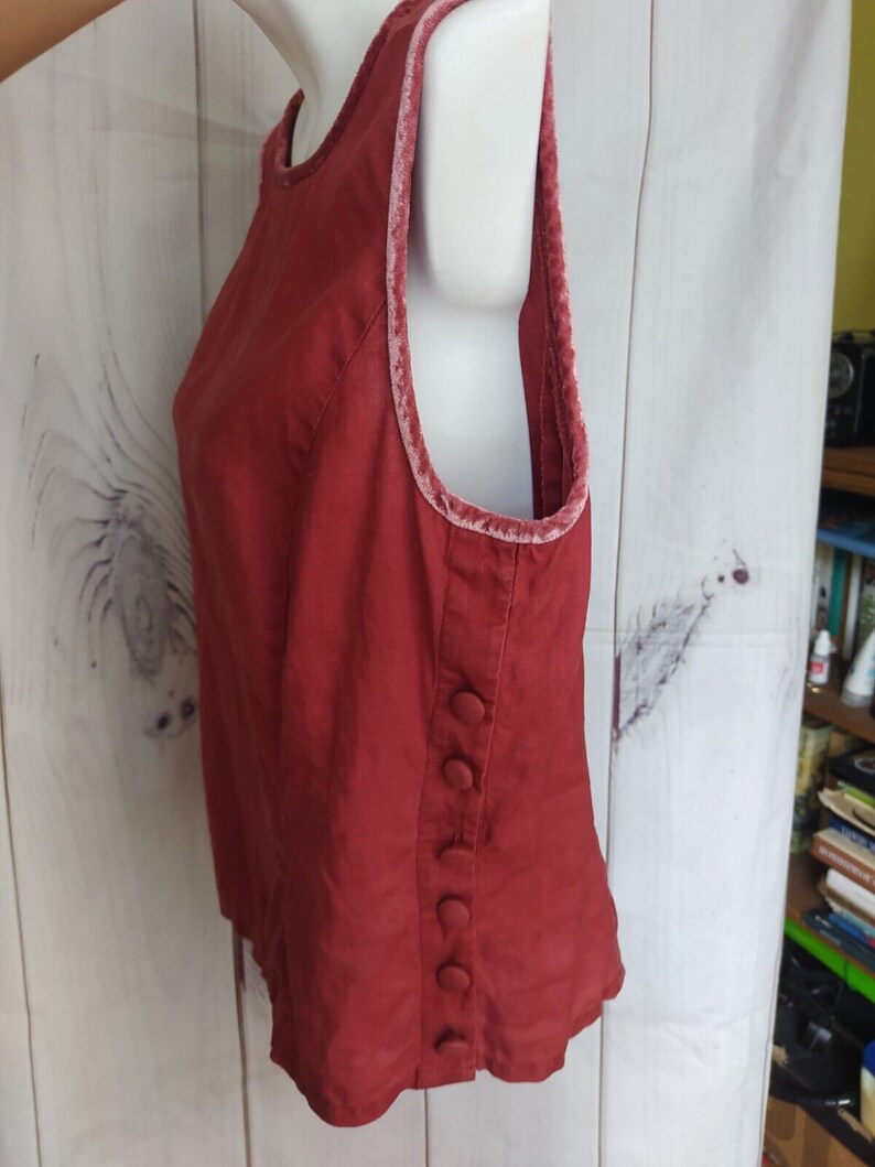 May include: A sleeveless, burgundy top with a velvet trim around the neckline and armholes. The top has a button closure on the side.