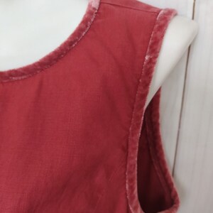 May include: Close-up of a red sleeveless top with a pink velvet trim around the neckline and armholes.