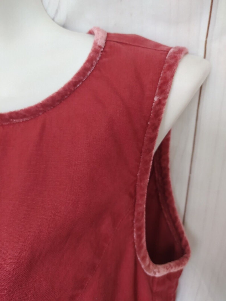 May include: Close-up of a red sleeveless top with a pink velvet trim around the neckline and armholes.