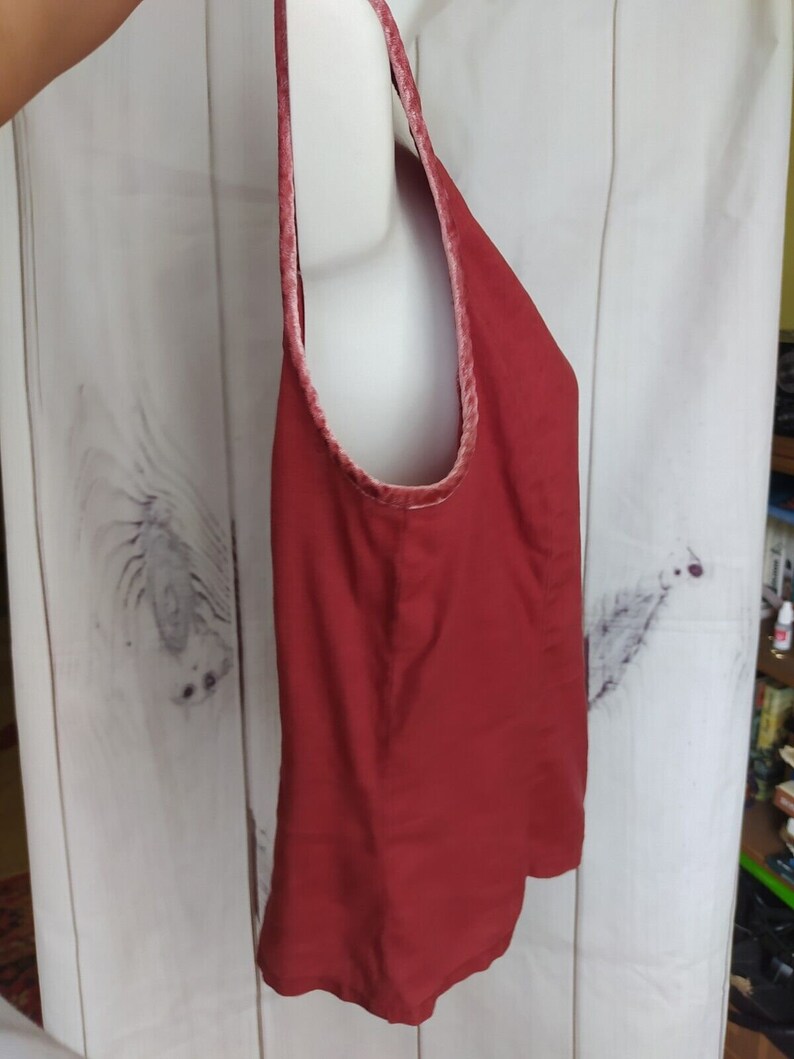 May include: A sleeveless red tank top with a velvet trim around the neckline. The top is made of a soft, lightweight fabric.