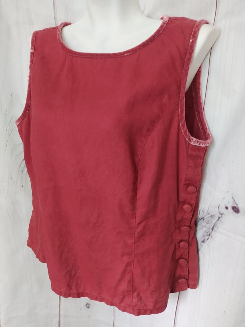 May include: A sleeveless red linen top with a velvet trim around the neckline and armholes. The top has a button closure on the side.