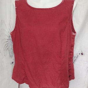 May include: A sleeveless red top with a velvet trim around the neckline and armholes. The top has a button closure on the side.