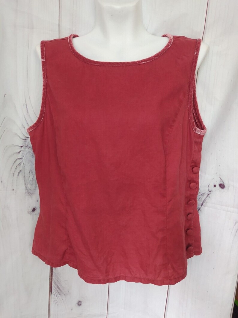 May include: A sleeveless red top with a velvet trim around the neckline and armholes. The top has a button closure on the side.